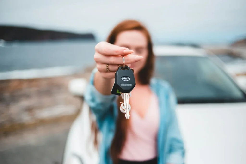 Young woman holding up car keys in front of a car